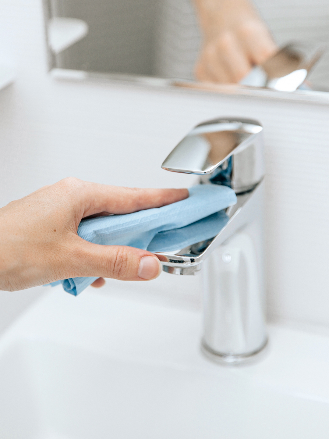 A person is wiping a chrome faucet with a blue cloth in a bathroom sink.